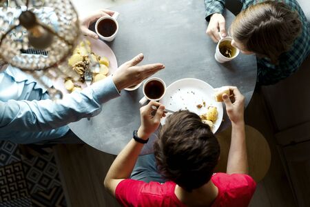 Family breakfast at the oval table by the window. Father and two sons eating potatoes and drinking coffee from white ceramic mugs. Top view through a crystal chandelier. Weekend Family Customs Conceptの写真素材
