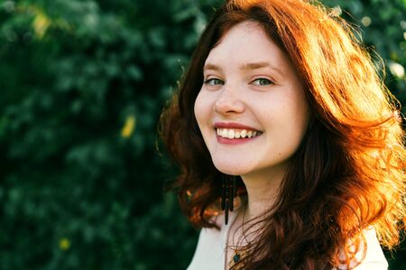 Beautiful young woman with red curly hair and freckles on her face. Close-up portrait. Yellow green summer backgroundの写真素材