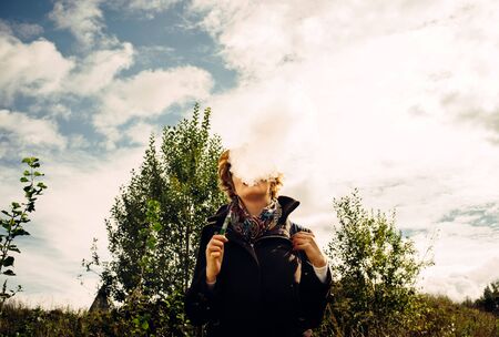 Charming girl with a short haircut in autumn clothes exhaling smoke from an electronic cigarette....