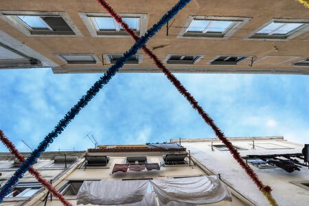 A view of the blue sky in the clouds through two rows of closely standing apartment buildings with clothes drying in the wind. Stretched out festive garlandsの写真素材