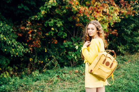 Cheerful smiling teenage girl of 14 years old with long curly red hair in a yellow sweater and with...