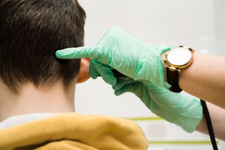 Preventive inspection of a teenage boy in a medical facility. Otorhinolaryngologist doctor pediatrician. Inspection of the sinuses of the nose with the reflector of the forehead and the nasal mirrorの写真素材