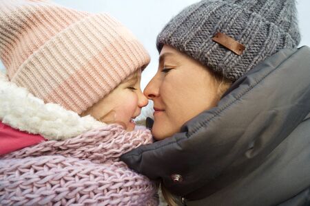 Daughter of four years and mother with warm winter clothes hats and scarves. Close-up portrait in...