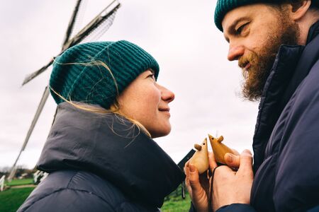 Loving couple man and woman face to face holding in hands symbol of their love two small wooden miceon the background of the mill. Rural spring landscape. Family Relations and Valentines Day Conceptの写真素材