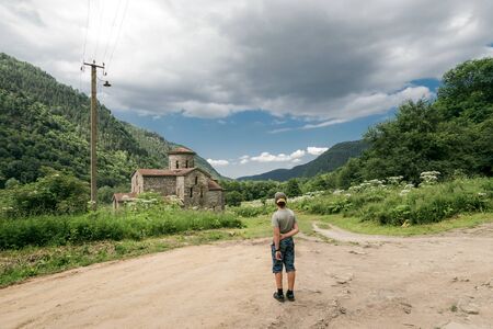 A boy standing at a crossroads in the mountains in front of an old Christian church. North Caucasus, Arkhyz Gorge. Rear view. Facelessの写真素材