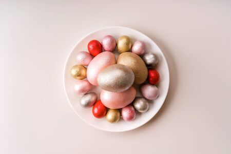 Colored painted pearl chicken and quail eggs of pink, red, silver, golden color on a purple plate pastel background. Minimalistic creative idea easter festive flat lay. Copy space for textの写真素材