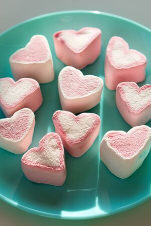 Heart shaped pink marshmallow lying on a blue turquoise plate. Valentines Day Party Concept. Treats guest children holiday birthday. Vertical banner social network and mobile phone screenの写真素材