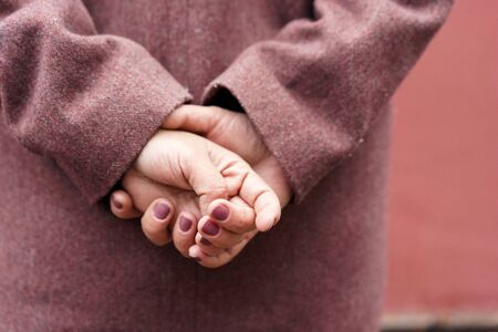Portrait of a woman hands in a burgundy coat view from the back against a red wall. The concept of minimalism in composition, without a face. Impersonal. Winter, snowflakesの写真素材