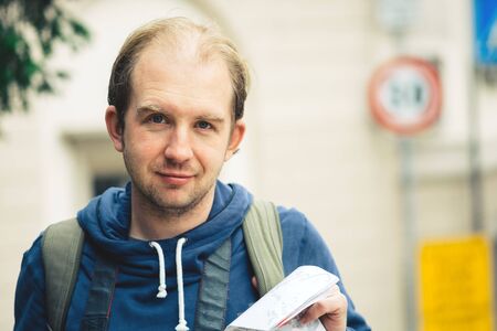 Closeup male portrait lonely traveler with a map in his hands and a backpack behind. Autumn spring clothes, weekend and travel conceptの写真素材