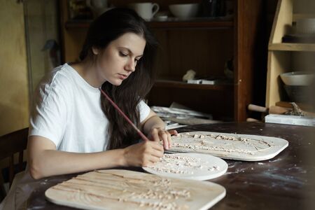 Woman hands brush with a brush the relief pattern obtained from the mold for casting clay products. Shaped method of preparing pottery. Handwork. Ceramic Making. Wall panelの写真素材