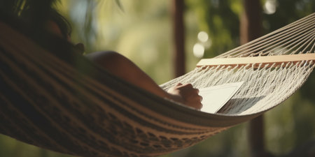A person enjoying a relaxing moment in a hammock while reading a book and soaking up the sun.の素材