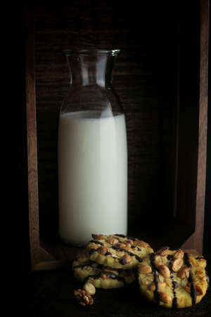 Chocolate cookies with nuts and  bottle of milk in dark wooden box.の写真素材