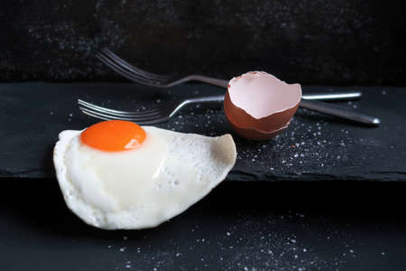 Fried egg with eggshell and forks on black board.の写真素材