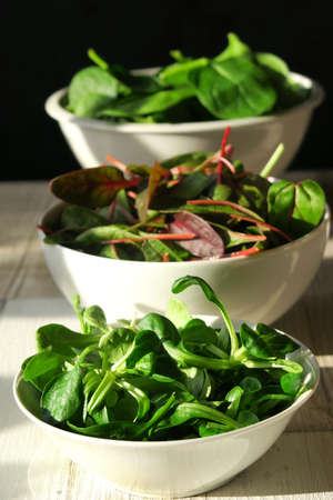 Three white bowls of fresh salads on wooden table. Baby spinach, mesclun and mache.の写真素材