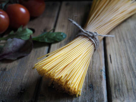 Bunch of spaghetti pasta tied with cord and fresh tomatoes on wooden desk.の写真素材