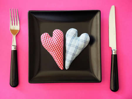 Two handmade textile hearts on black table on pink background.の写真素材