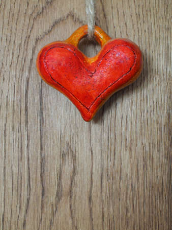 Red handmade heart hanging on cord on wooden background.の写真素材