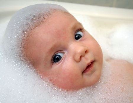 A baby in a bathtub with soap foam.