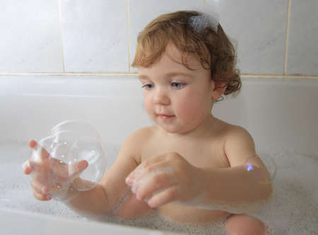 A child playing with soap foam in a bathtub.