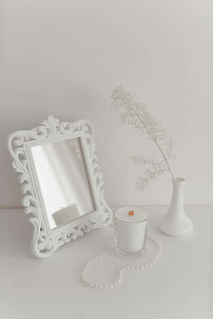 White decorative branch in a vase with a mirror and a candle stand on a table