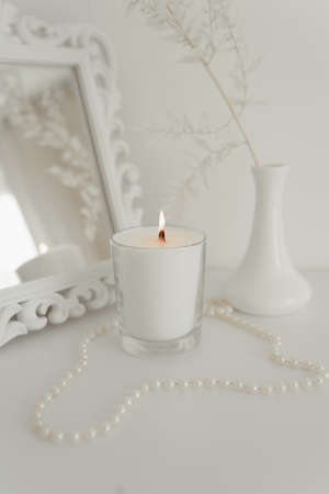 White decorative branch in a vase with a mirror and a candle stand on a tableの写真素材