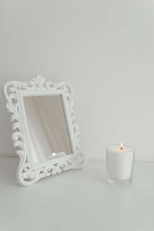 Burning white candle with a wooden wick and a white mirror on a white backgroundの写真素材