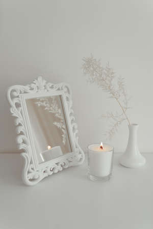 White decorative branch in a vase with a mirror and a candle stand on a tableの写真素材