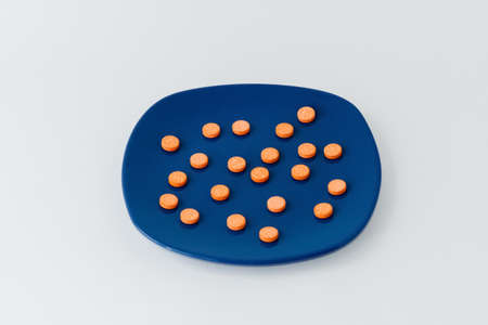 Medical orange pills lie on a blue plate on a white background