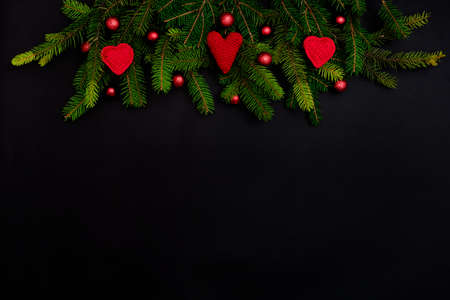 Branches of a Christmas tree with red hearts red Christmas decorations on a black background with copy space.の写真素材