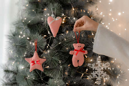 A female hand hangs a handmade bear toy on the Christmas tree. Handmade toys bear, heart and star.の写真素材
