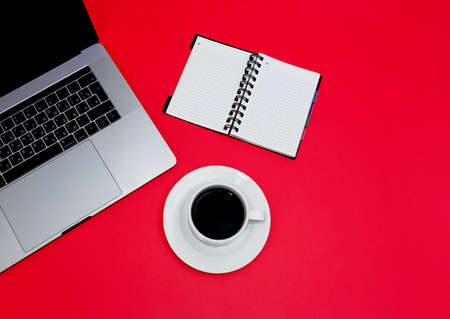 Laptop with coffee cup and notepad on red background. Flat layout with copy space.の写真素材