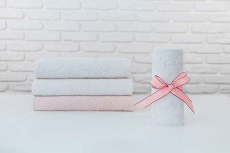 Rolled up towel with pink ribbon. Stack of clean soft towels on brick wall background.の写真素材