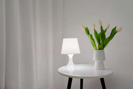 White tulips in a vase on a table with a table lamp with copy spaceの写真素材