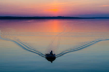 The boat floats on the sea in the evening in the sunset light leaving the waves.の写真素材