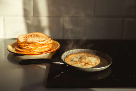Cooking thin pancakes on an induction oven in the sun, steam comes from the pancake.の写真素材