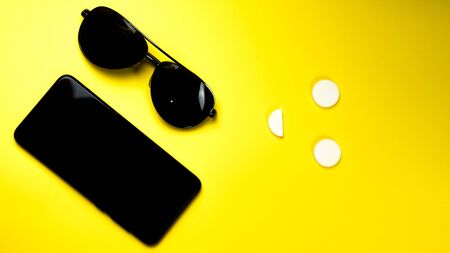 black phone sunglasses on yellow background. top view copy space