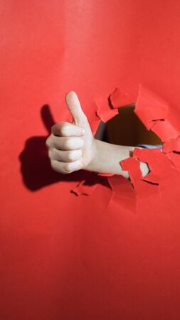child's hand with hole red background, holds finger up.の写真素材