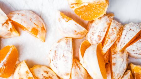 Close-up of pieces of orange without peels in white snow and with sun light.の写真素材