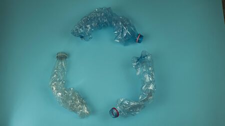 Three crashed plastic bottles on blue background form resycling sign. Plastic utilisation concept....