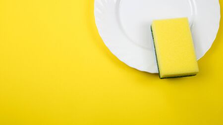 Cleaning sponge on a white plate on a yellow background.