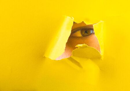 A manly eye looks through a hole in a paper yellow background.の写真素材