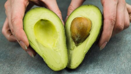 sliced avocado in the hands of a woman, on a gray concrete background.の写真素材