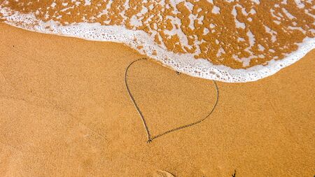 Heart drawn on the beach sand with sea foam and wave. top view. copy spaceの写真素材