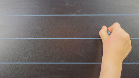 schoolboy hand writes in chalk on a blackboard during a lesson at schoo.