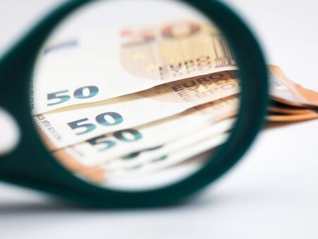Banknotes of 50 euros under a magnifying glass on a white background.