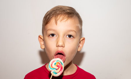 a boy eats a sweet multicolored candy on a stick, a boy with a lollipop of sugar, which he holds in his handsの写真素材