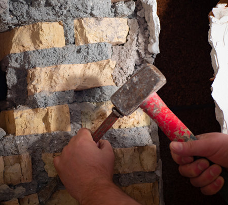 worker with a hammer and chisel makes a hole in the wall at the construction siteの写真素材