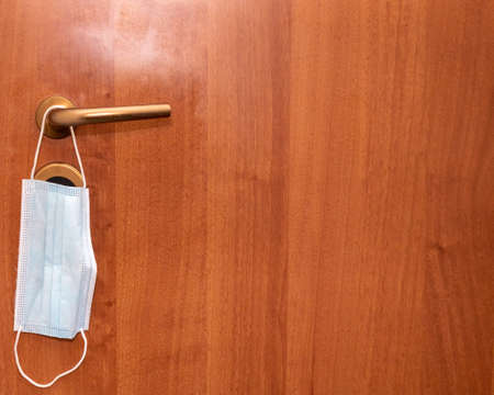 medical mask for protection from virus hanging on the door handle on the door to the room or office,...