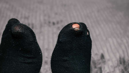Children hands playing with his toes sticking out of socks, Old socks on boy feet, Pair of socks with hole and a finger sticking out of them. kid boy with worn out socks sitting in bedの写真素材