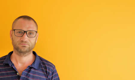 Waist-up shot of happy and satisfied handsome young man wearing glasses over yellow background, tilting head, smiling and laughing, looking friendly at camera right with copy spaceの写真素材